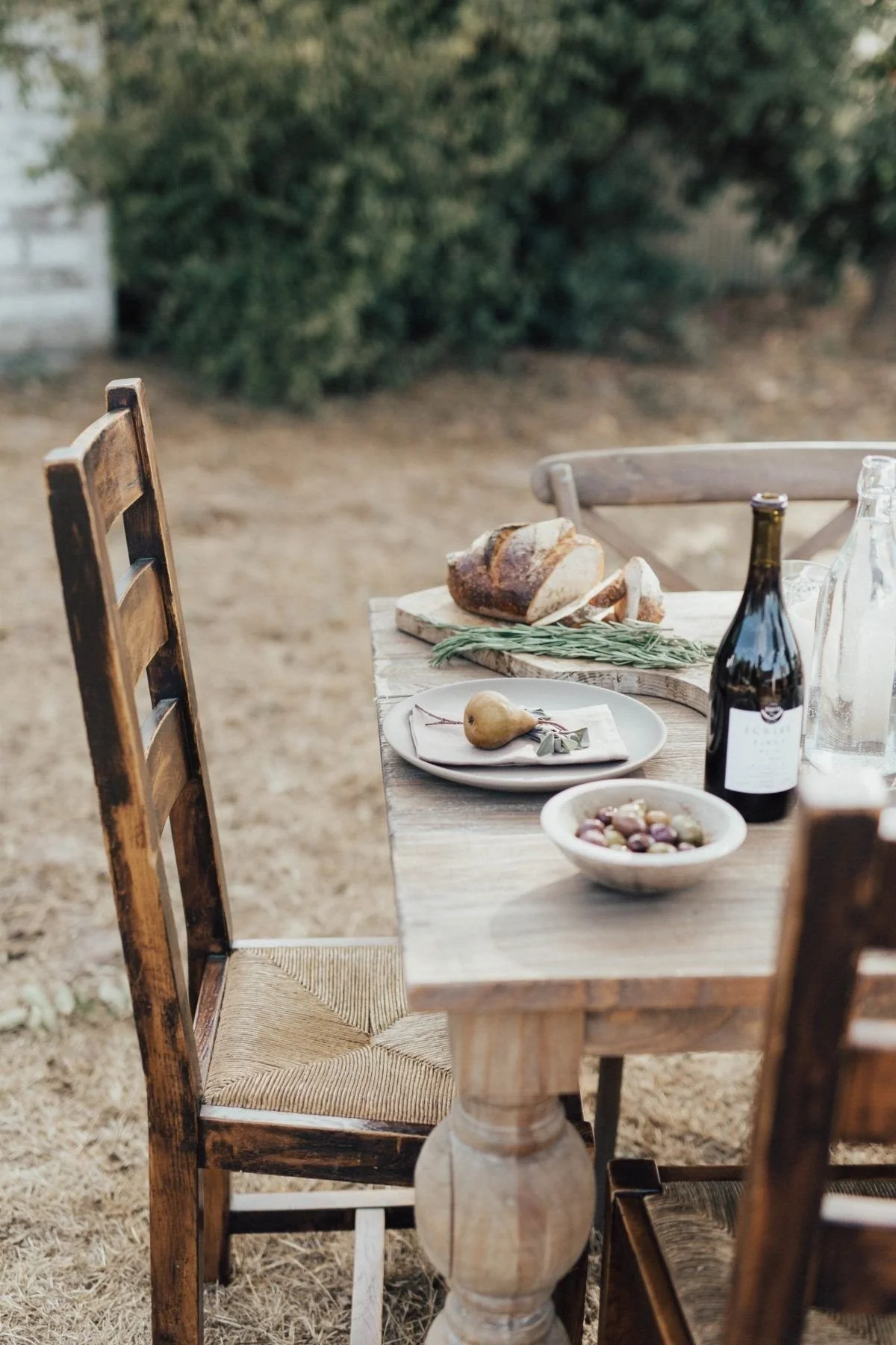 Outdoor farmhouse table set with bread, wine, olives, and pears